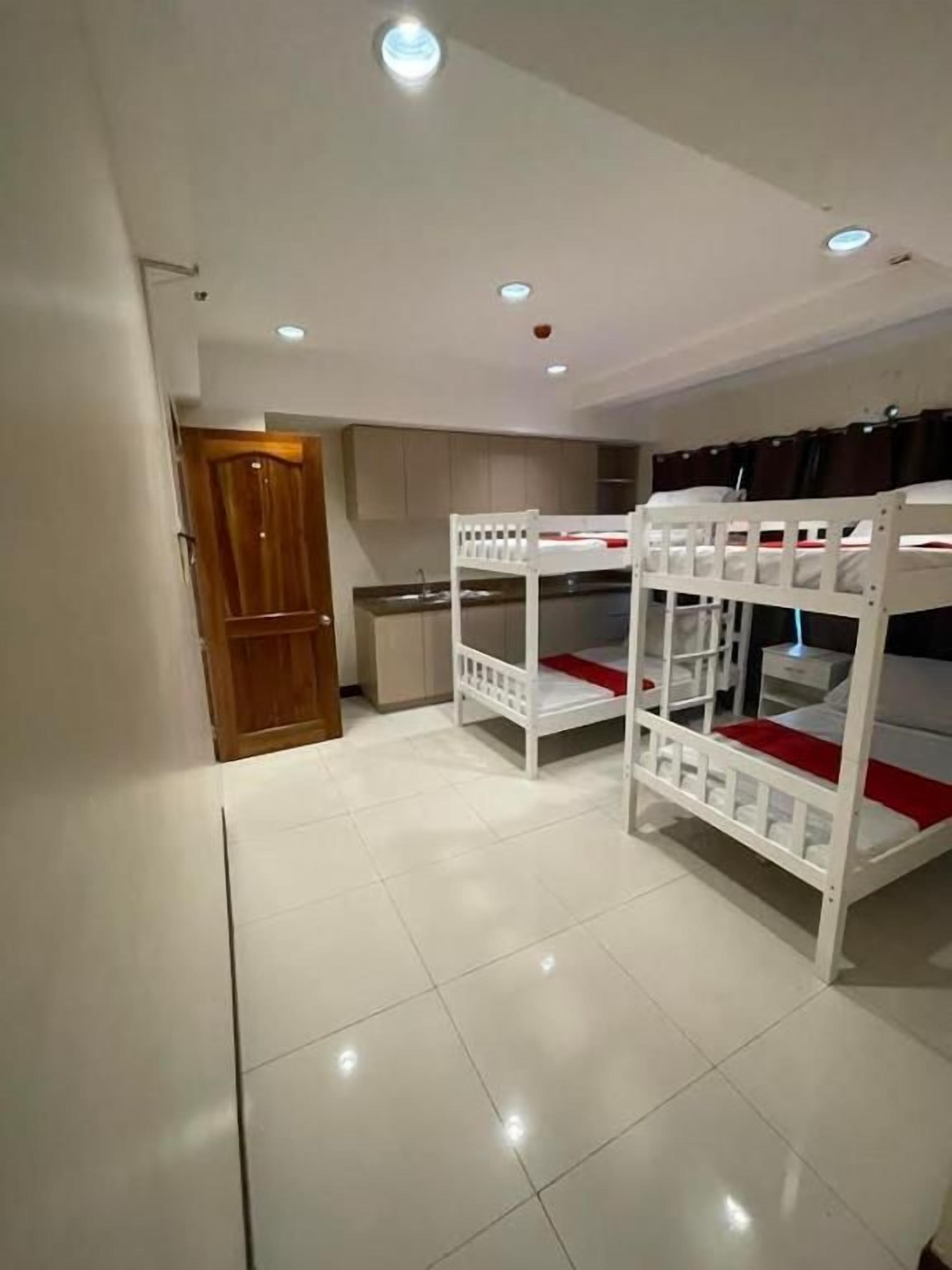 A room with bunk beds, a wooden door, and a kitchen area.