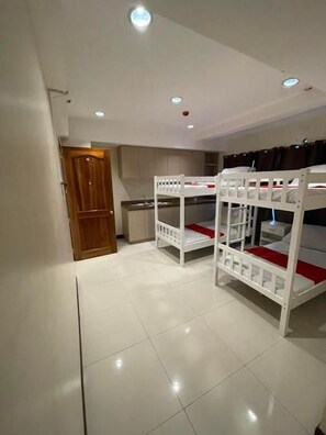 Una habitación con literas, una puerta de madera y una zona de cocina.