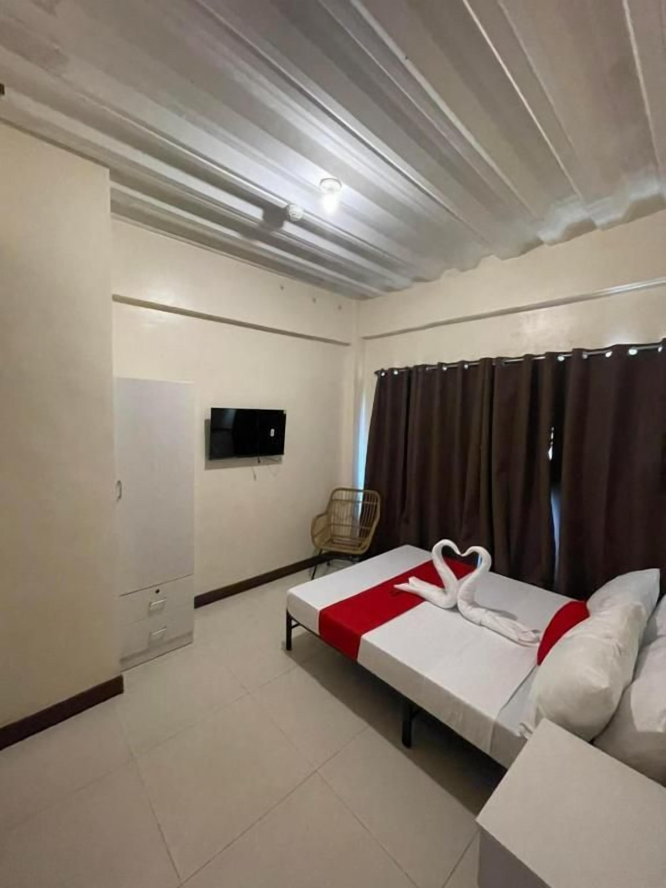 A hotel room with a bed, a television, a chair, and a window with curtains.