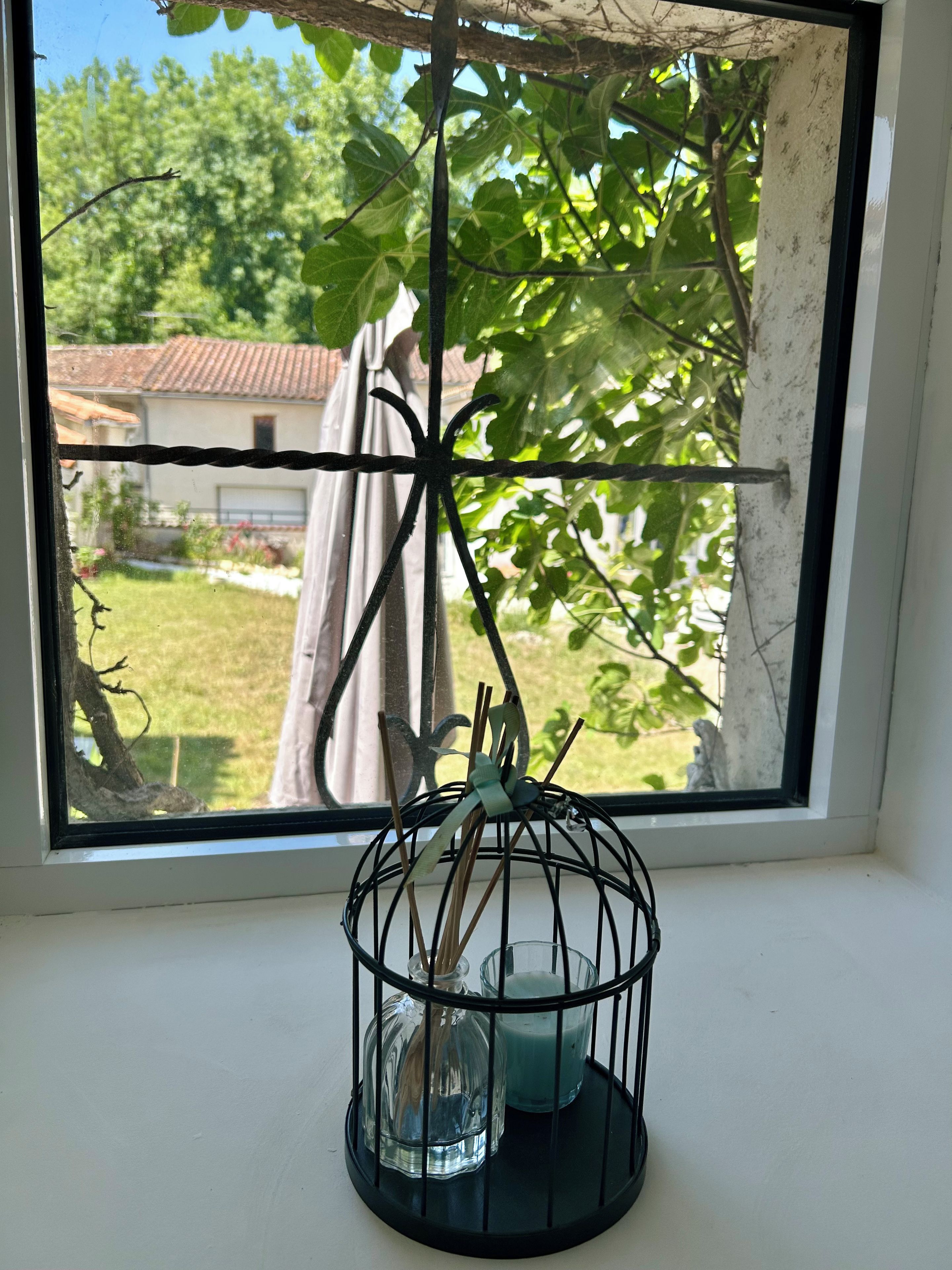 Ein Fenster mit einem Vogelkäfig aus Metall, der eine Kerze und eine Glasflasche enthält.