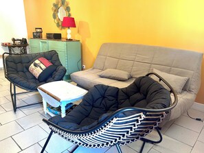 A room with a grey sofa, a black armchair, and a wicker chair with a white table.