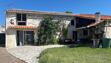 Un bâtiment à deux étages, doté d’un toit en tuiles, d’une façade en pierre et d’un petit jardin avec de la pelouse et un arbre.
