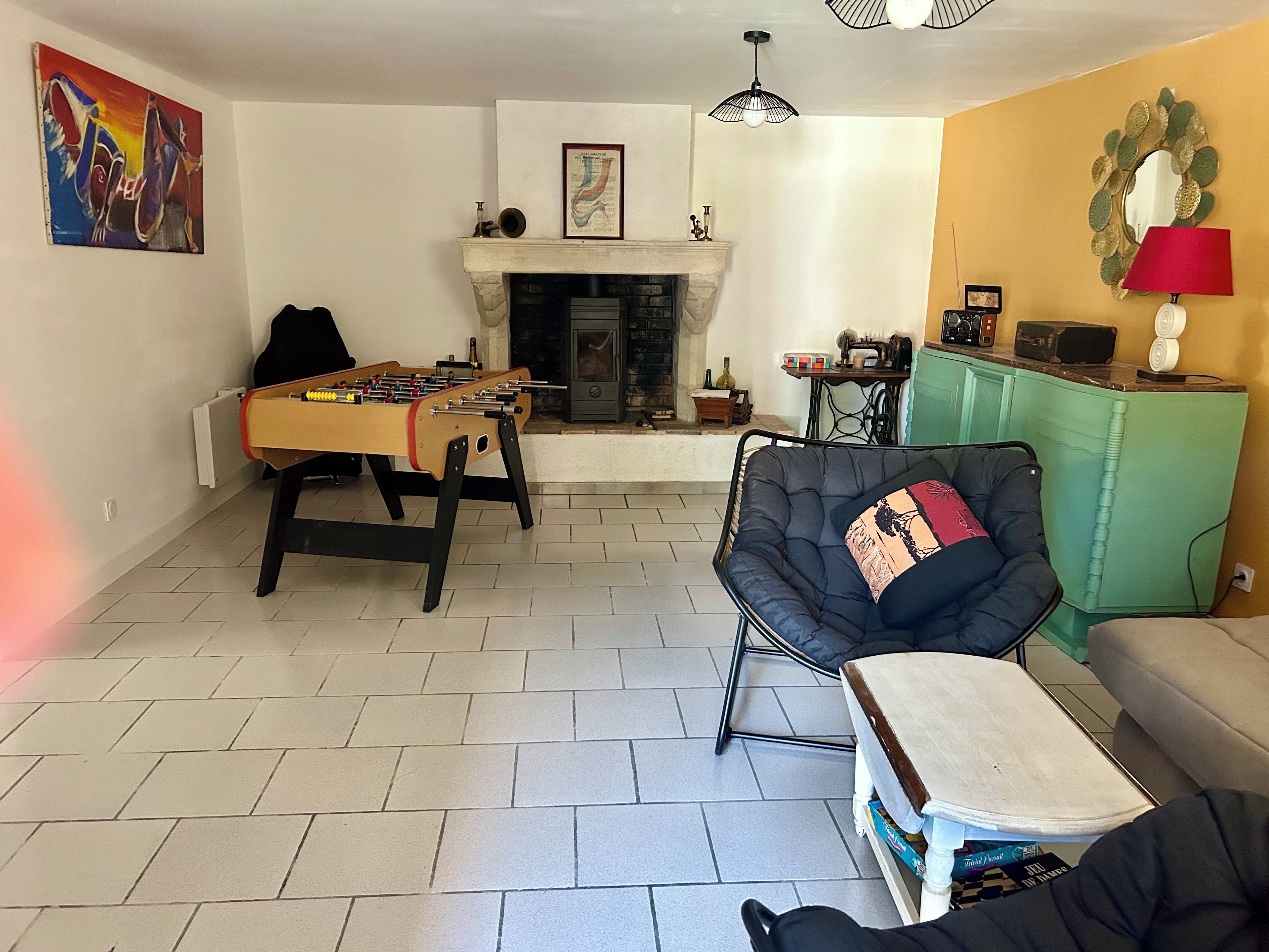 Ein Wohnzimmer mit einem Kicker, einem Sofa, einem Sessel, einem Kamin und einem grünen Schrank.