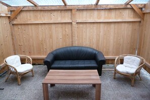A wooden deck with a black leather sofa and two wicker chairs. - Holiday apartment with 1 bedroom (Freudenstadt)