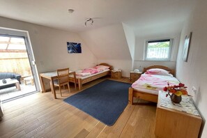 A bedroom with a bed, a desk, a chair, a small table with a vase, and a window. - Holiday apartment with 1 bedroom (Freudenstadt)