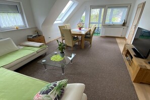 Ein modernes Loft-Apartment mit Essbereich, einer Couch, einem Fernseher und einem großen Fenster.