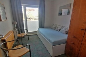 Un dormitori amb un llit, escriptori, dues cadires, una commode i una finestra amb cortines.