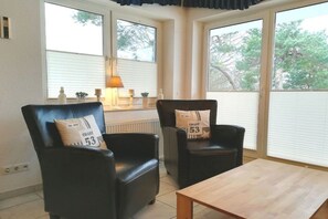 A room with two black leather chairs, a wooden table, and large windows with blinds. - Holiday apartment with 2 bedrooms (Seebad Heringsdorf)