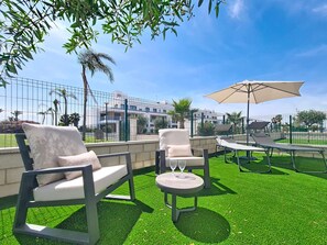 An outdoor seating area with chairs and a table, surrounded by a green lawn and a fence. - Ground Floor Apartment Overlooking the Pool (Los Alcazares)