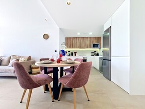 A modern kitchen with a dining area, featuring a round table with chairs, a sofa, and a refrigerator. - Ground Floor Apartment Overlooking the Pool (Los Alcazares)