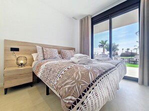 A modern hotel room with a large bed, a bedside table with a lamp, and a view of the outdoors. - Ground Floor Apartment Overlooking the Pool (Los Alcazares)