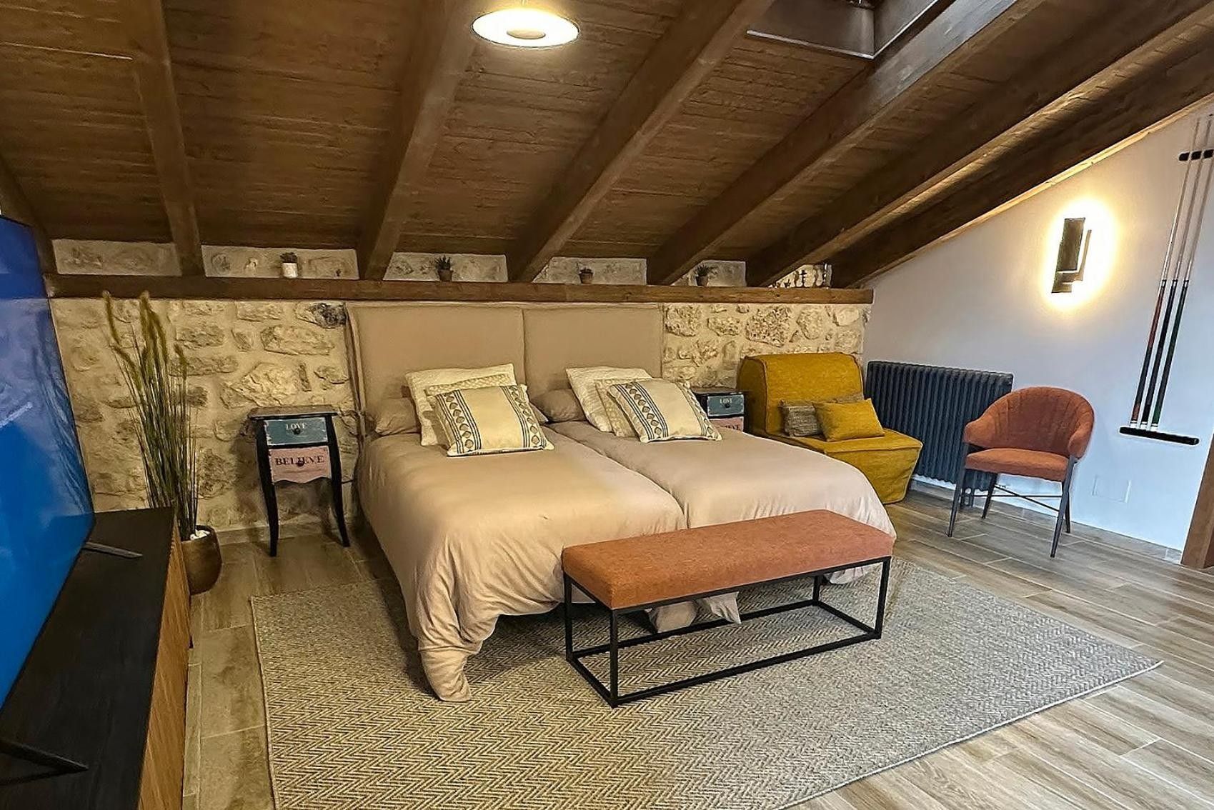 A bedroom with a bed, a bench, a chair, a small table, and a potted plant.