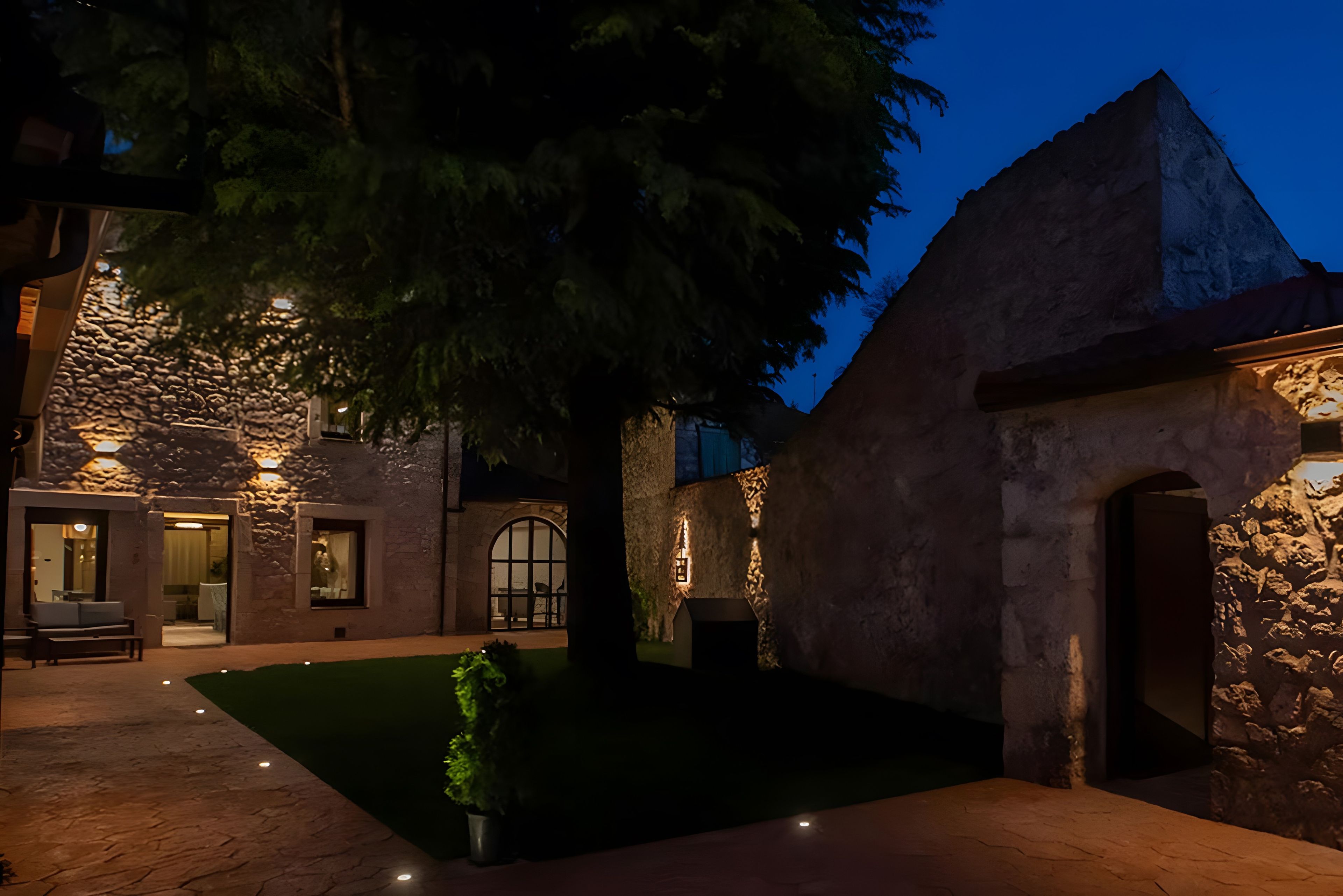 Un edificio de piedra con un patio, un árbol y una entrada bien iluminada.