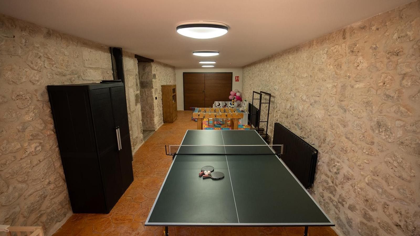 Een kamer met een tafeltennistafel, een tafelvoetbaltafel en een houten kast.