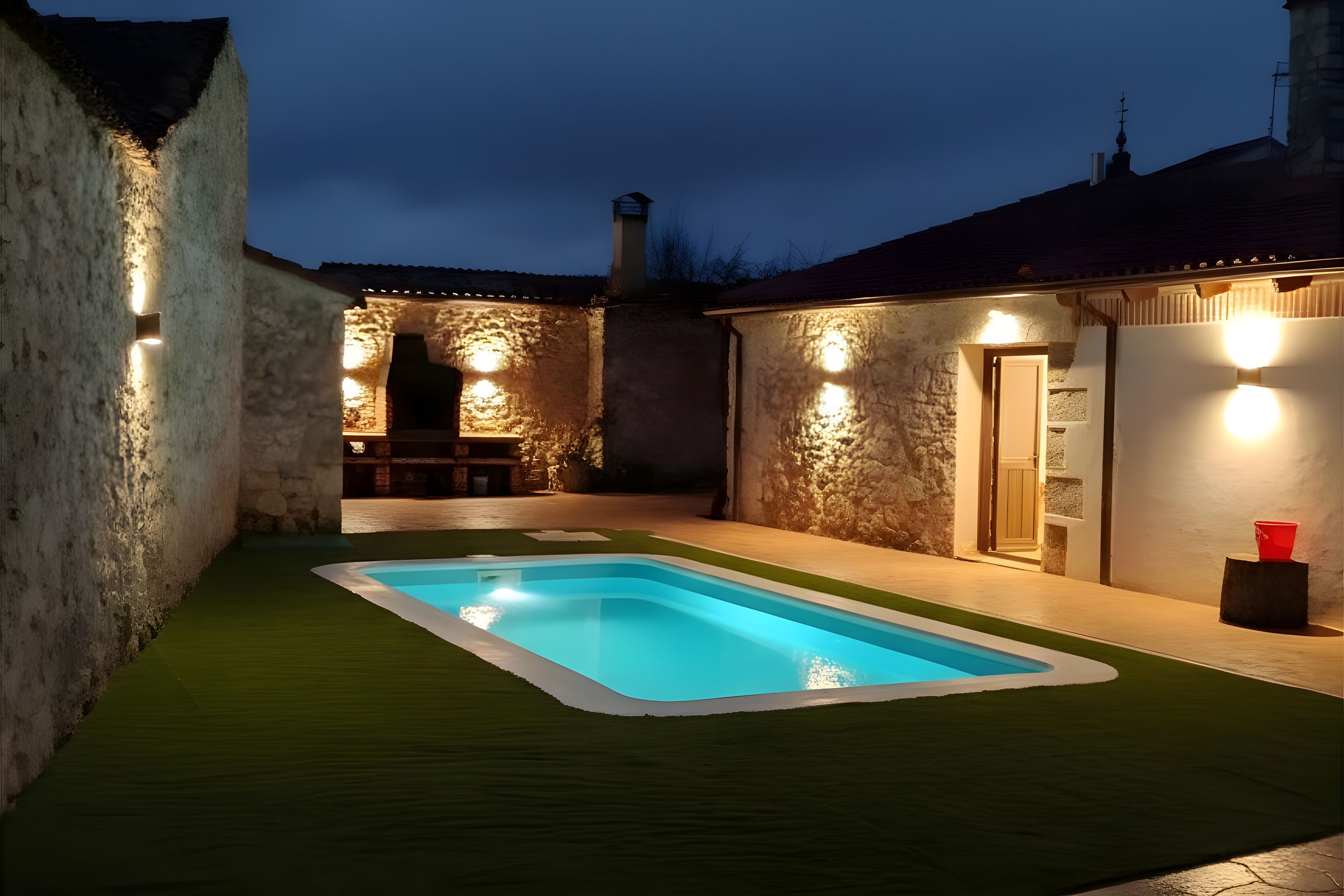 A swimming pool with artificial grass, surrounded by stone walls and illuminated by exterior lights.