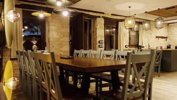 Un comedor con mesa y sillas de madera, iluminación colgante y pared de piedra.