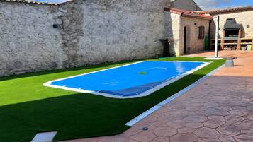 A swimming pool with artificial grass, a stone wall, and a tiled patio.
