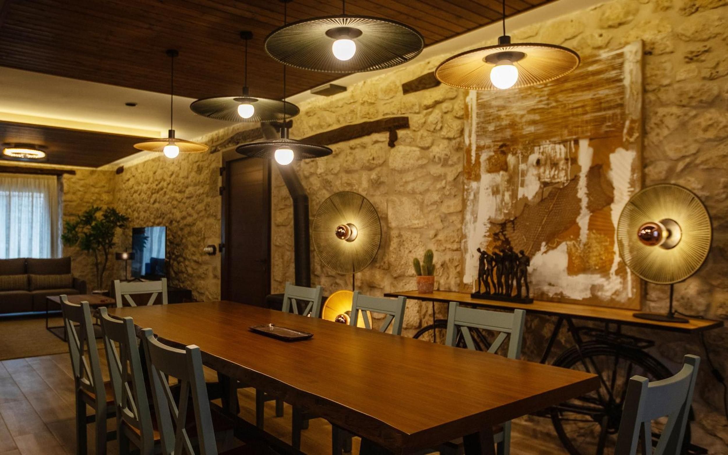 Un espace repas avec une longue table en bois, plusieurs chaises et des luminaires suspendus.
