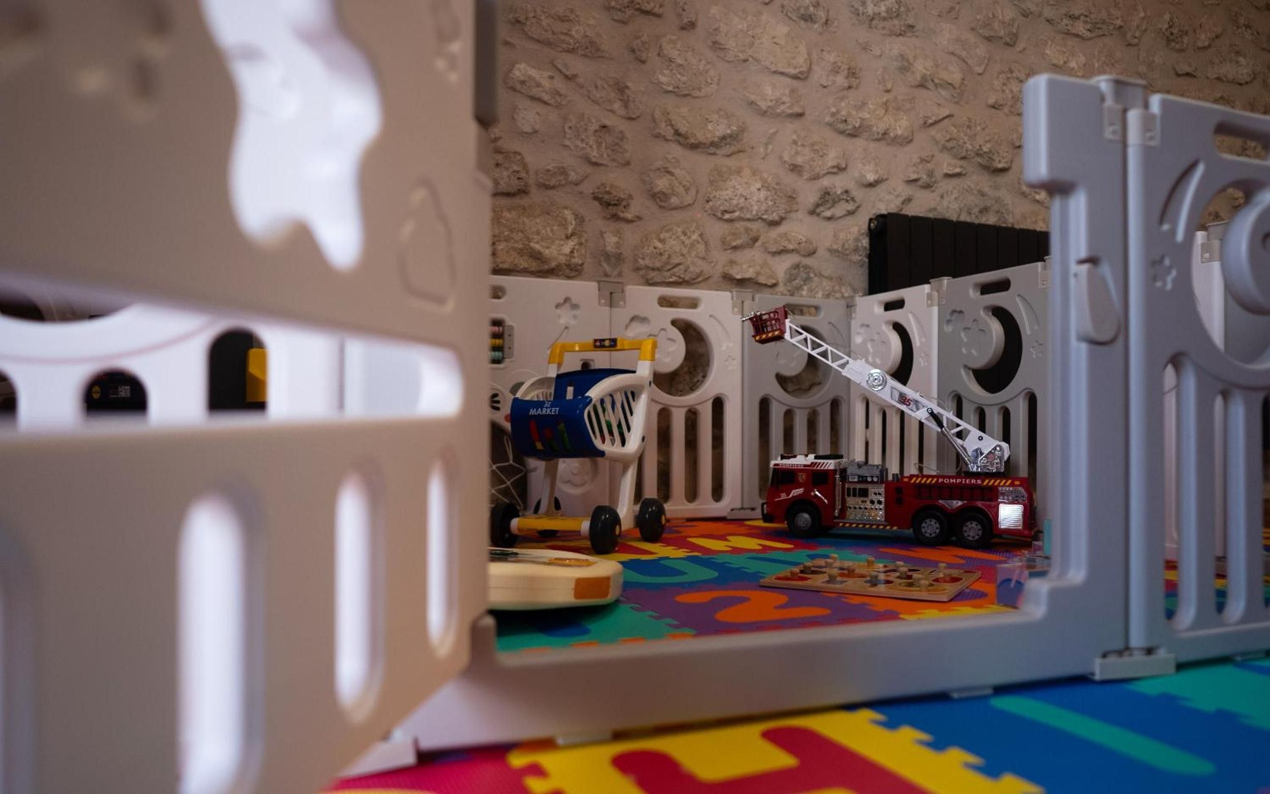 A play area with a toy fire truck, a toy ladder, and a toy market stall.