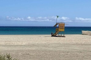 A lifeguard tower with a flag on a sandy beach with the ocean in the background. - Casa Blanka Bahia Playa (Costa Calma)
