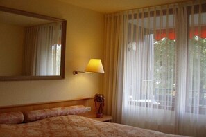 Ein Hotelzimmer mit einem Bett, einer Nachttischlampe, einem Spiegel und einem Fenster mit Vorhängen.