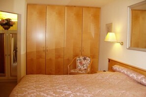 A bedroom with a large wardrobe, a chair, a bed with a patterned bedspread, and a wall-mounted lamp. - Holiday apartment with 2 bedrooms (Bad Herrenalb)