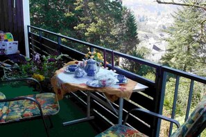 A balcony with a table set for tea, surrounded by chairs, overlooking a scenic view of trees and buildings. - Holiday apartment with 2 bedrooms (Bad Herrenalb)