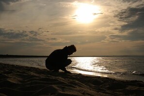 A silhouette of a person crouching on a sandy beach with the sun low on the horizon. - Holiday apartment with 2 bedrooms (Waren-Müritz)