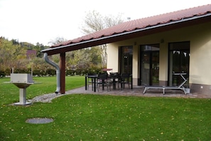 Ein überdachter Außenbereich mit Tisch, Stühlen, einer Bank und einem Mülleimer.