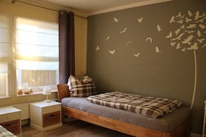 Ein Schlafzimmer mit einem Einzelbett, einem Nachttisch, einer Lampe und einem Fenster mit Vorhängen.