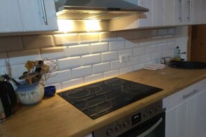 A kitchen with a black induction cooktop, white cabinets, and a wooden countertop. - Beautiful wooden cabin in a green meadow (Jabel)