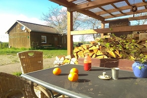 A covered outdoor seating area with a table, chairs, and a rustic wooden building in the background. - Beautiful wooden cabin in a green meadow (Jabel)