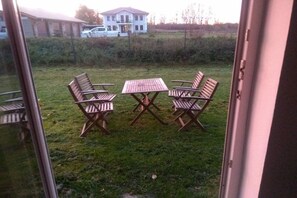A view through a glass door of a grassy outdoor area with a table and four chairs. - Beautiful wooden cabin in a green meadow (Jabel)