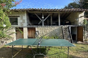 A stone house with a tiled roof, a ping pong table in the front yard, and a ladder leaning against the house. - Holiday home in Lusignac with swimming pool (Lusignac)