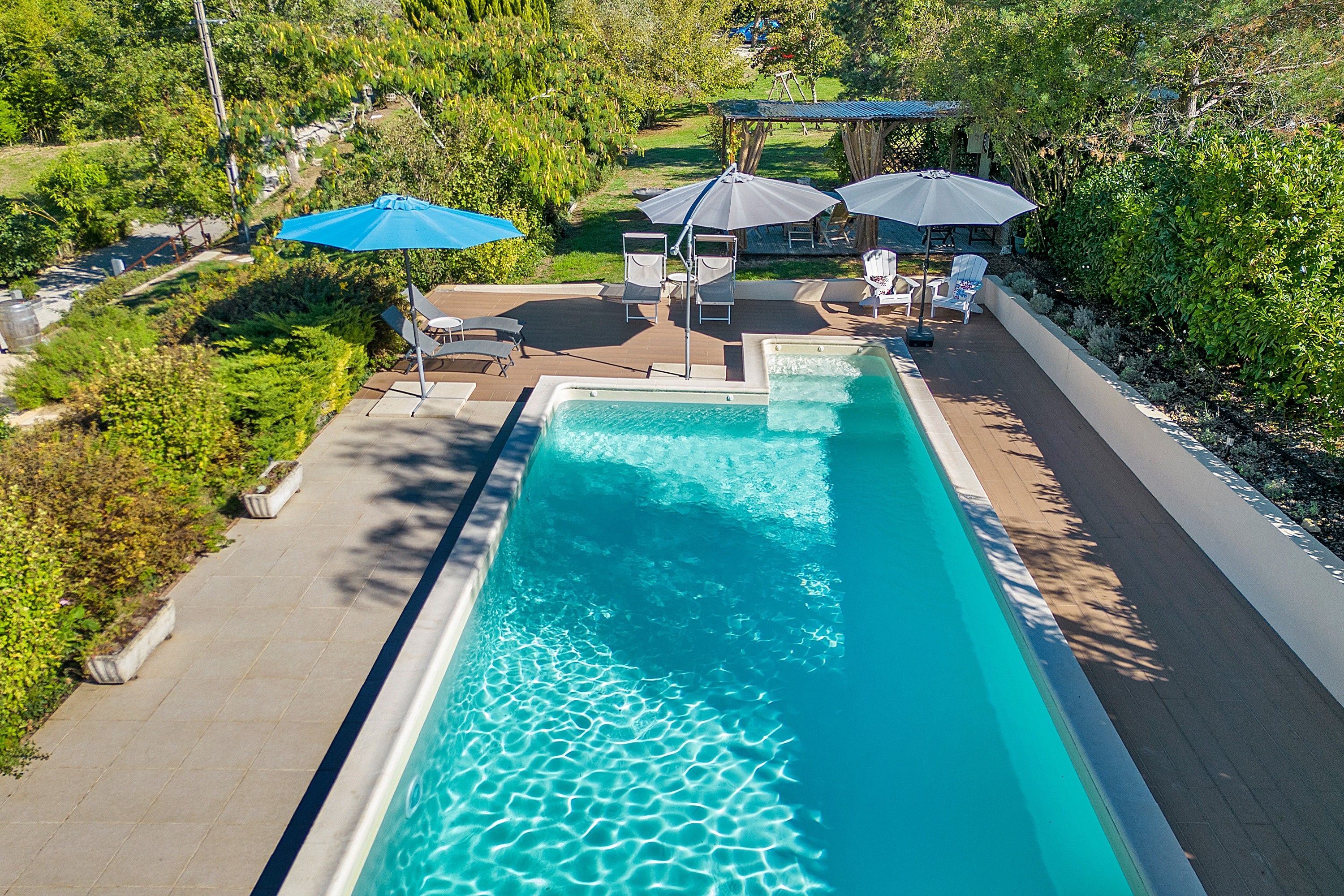 A rectangular swimming pool with clear blue water, surrounded by a paved deck.