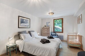 Quarto com cama, mesas de cabeceira, penteadeira, cadeira, berço, janela e luminária de teto.