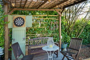 A wooden pergola with a dartboard, a table, and two chairs in a garden setting. - Holiday Home 'Maison Joie de Vivre' with Large Fenced Garden, Private Pool, Terraces and AC (Cénac-et-Saint-Julien)
