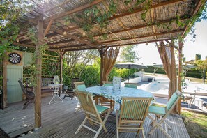 Um pátio externo com mesa redonda e cadeiras, uma pérgola com cobertura de tecido e um alvo de dardos.