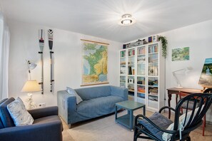 A living room with a sofa, a chair, a small table, a bookshelf, a map on the wall, and a lamp. - Holiday Home 'Maison Joie de Vivre' with Large Fenced Garden, Private Pool, Terraces and AC (Cénac-et-Saint-Julien)
