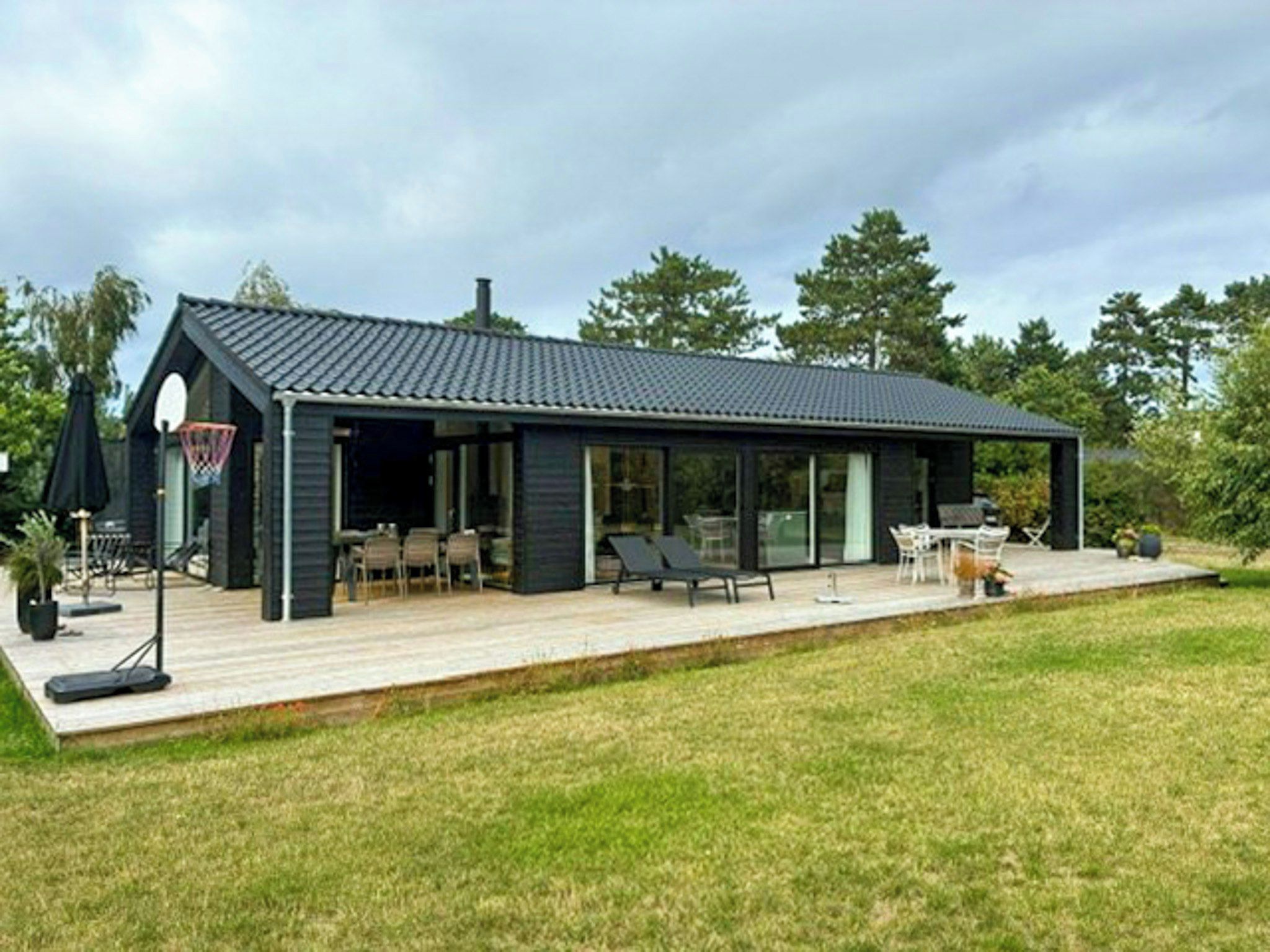 A modern house with a deck, outdoor seating, and a basketball hoop.