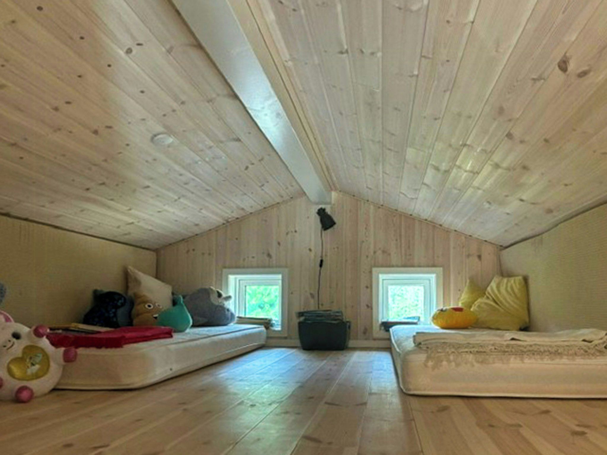 Una piccola stanza mansardata con travi di legno a vista, due finestre e un materasso per terra.