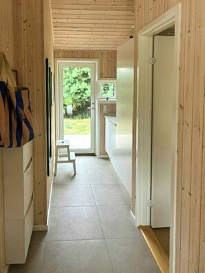 A narrow hallway with wooden walls, a white door at the end, and a small stool in the center.