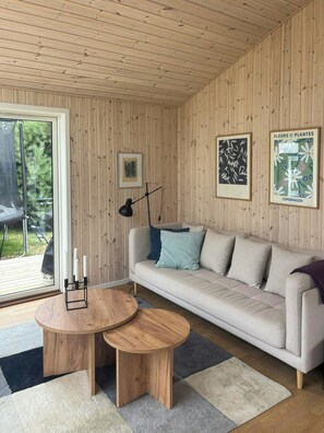 Habitació amb paret de fusta panelada, un sofà, una taula de centre rodona de fusta, una làmpada de peu i quadres emmarcats.