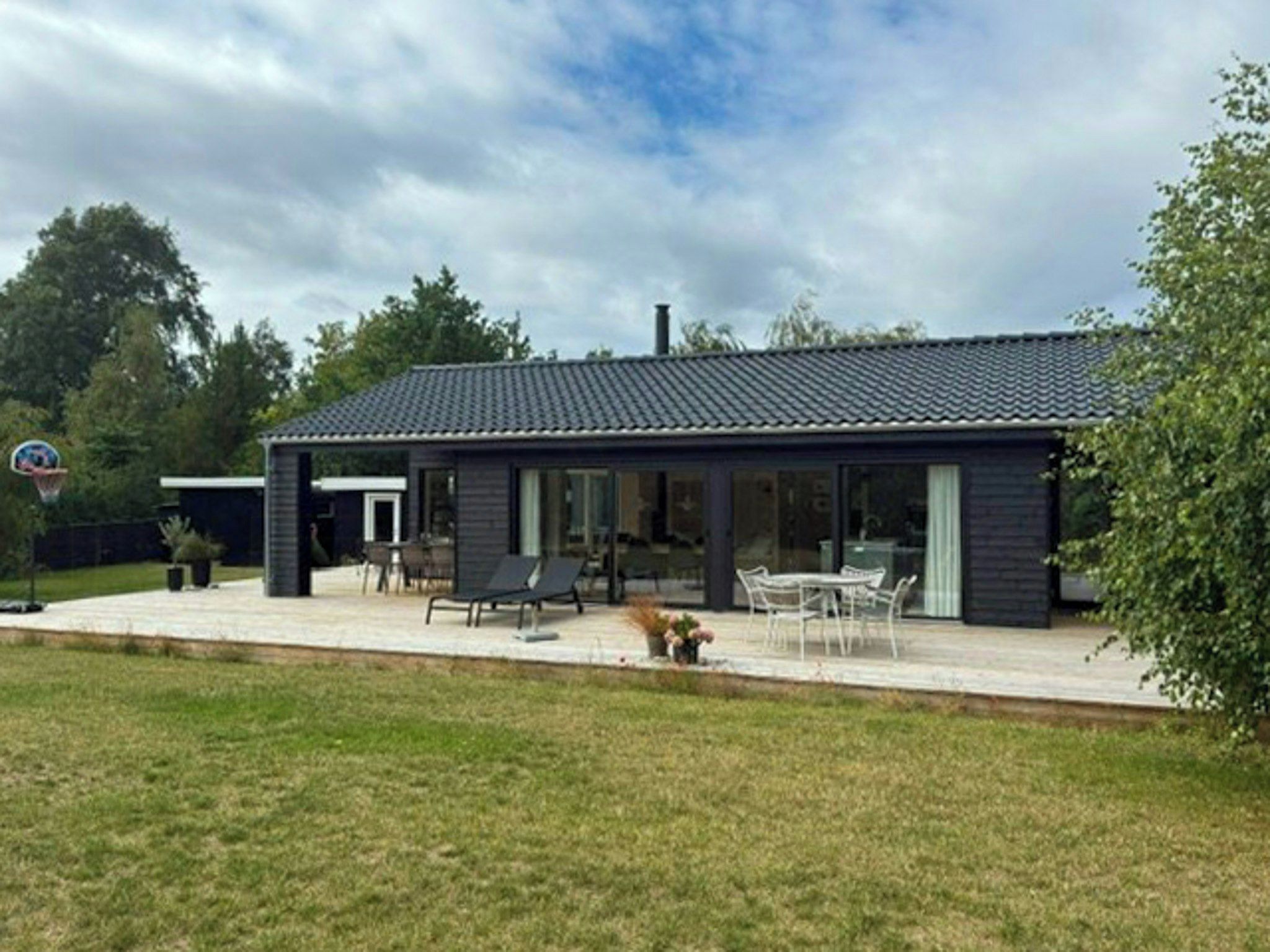 A modern two-story house with a covered patio, a basketball hoop, and a garden.