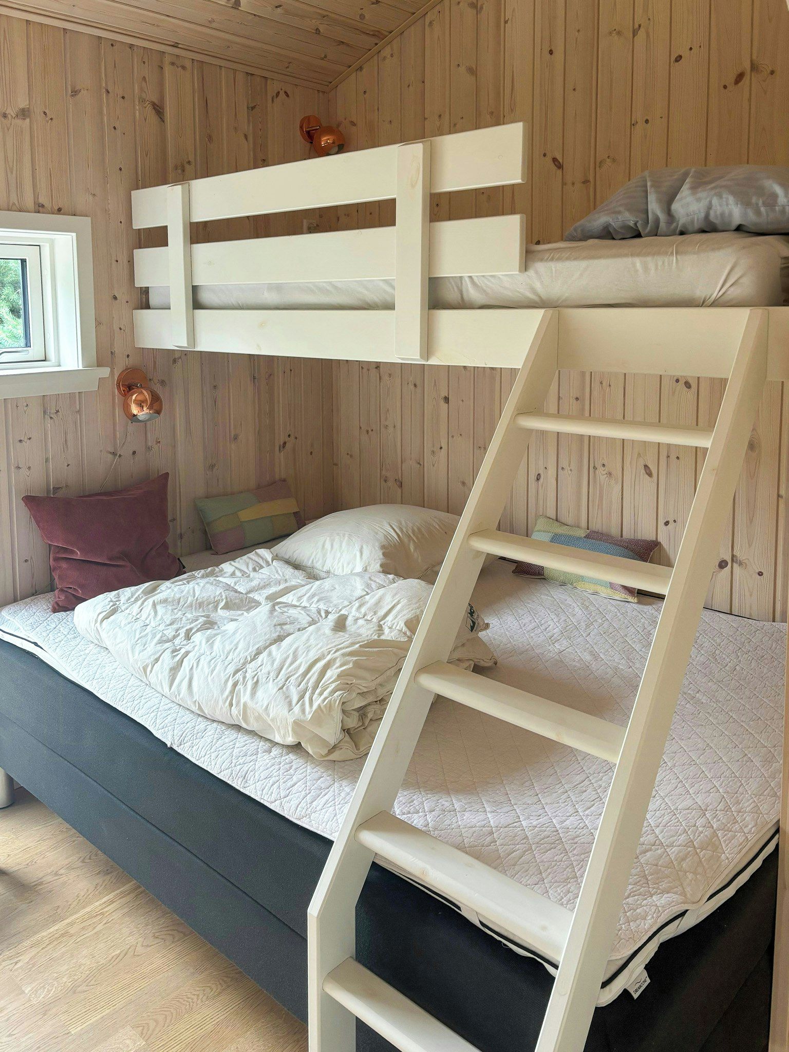 Ein Etagenbett mit einer Leiter, ein Fenster mit Vorhängen und eine Holzwand.