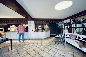 A modern kitchen with white cabinetry, a central island, and a person standing by the counter. - Superior apartment Goldener Hahn (Baiersbronn)