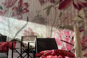 Ein Zimmer mit floralem Wandpapier, einem schwarzen Stuhl und einer roten Decke.
