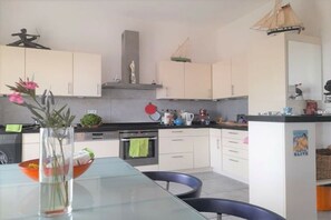 A modern kitchen with white cabinets, a glass dining table, and a variety of kitchen appliances. - mas de perimont || St.Pierre la mer (St.Pierre la mer)