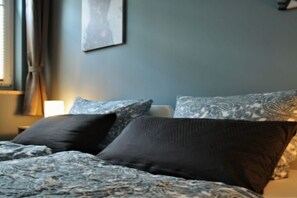 Ein Bett mit gemusterten Betttextilien, eine Nachttischlampe und ein Wandbild.