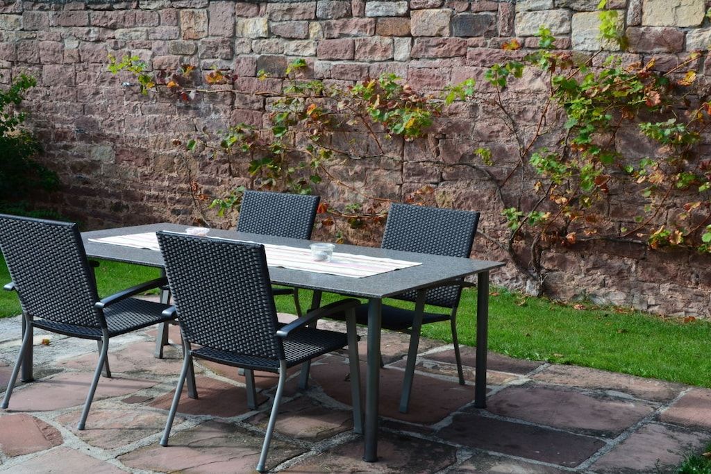 A stone patio with a table and chairs, a brick wall, and some ivy.